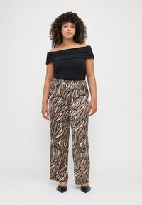 Μαύρο τοπ με ανοιχτούς ώμους και λεπτομέρεια συγκέντρωσης, συνδυασμένο με ροή παντελόνια σε καφέ και λευκό μοτίβο σπείρας, και μαύρες στιλέτο παπούτσια.