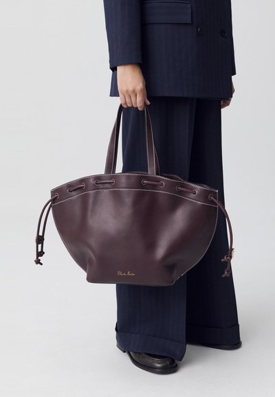Borsa a tracolla in pelle di un intenso borgogna con una forma arrotondata. Presenta cuciture a contrasto, lacci sui lati e due manici resistenti.