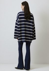 Pull oversized rayé marine avec des rayures blanches horizontales, tricot texturé, associé à un jean en denim foncé évasé et des bottines noires.