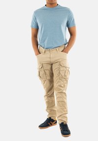 Lichtblauw T-shirt met ronde hals, gecombineerd met beige cargobroeken met meerdere zakken. Zwarte sneakers met oranje accenten maken de look compleet.