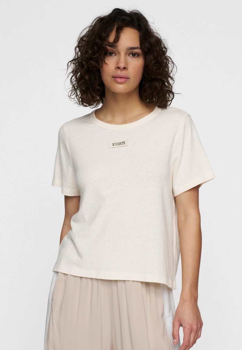 Crèmekleurig kortarm T-shirt van zacht materiaal, met een ronde halslijn en een klein label met "10DAYS" geborduurd op de voorkant.
