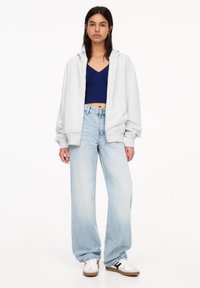 Hellgrauer oversized Hoodie, marineblaues Crop-Top, hellblaue High-Waist-Jeans und weiße Sneakers mit schwarzen Streifen; lässiger Streetwear-Look.