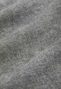 Lähikuva pehmeästä, harmaasta neulotusta kankaasta, jossa näkyy tekstuuri ja lempeitä laskoksia.