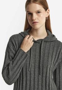 Szara bluza z kapturem o prążkowanej teksturze, z długimi rękawami i sznurkiem do regulacji kaptura. Materiał wygląda na miękki i lekki, z delikatnymi detalami.