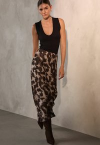 Schwarzes ärmelloses Top kombiniert mit einem braunen Leopardenmuster-Rock, der eine drapierte Silhouette aufweist, und hohen braunen spitzen Stiefeln.