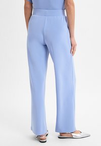  Lichtblauwe, wijde broek met een gladde textuur en een elastische tailleband. Gecombineerd met zwarte en zilveren instappers.