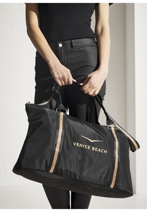 Schwarze Nylon-Duffeltasche mit goldenen Akzenten und dem Aufdruck "VENICE BEACH." Sie verfügt über zwei Tragegriffe und ein geräumiges Hauptfach.