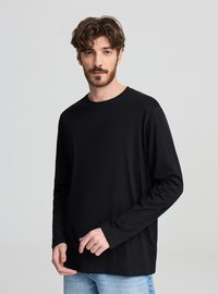 Czarna koszulka z długim rękawem i okrągłym dekoltem, wykonana z gładkiej tkaniny o luźnym kroju. W połączeniu z jasnoniebieskimi jeansami.