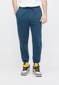 Μπλε παντελόνι τζόγκινγκ από απαλό υλικό με ελαστική μέση και κορδόνι, διαθέτει πλαϊνές τσέπες και στενόμακρα πόδια.