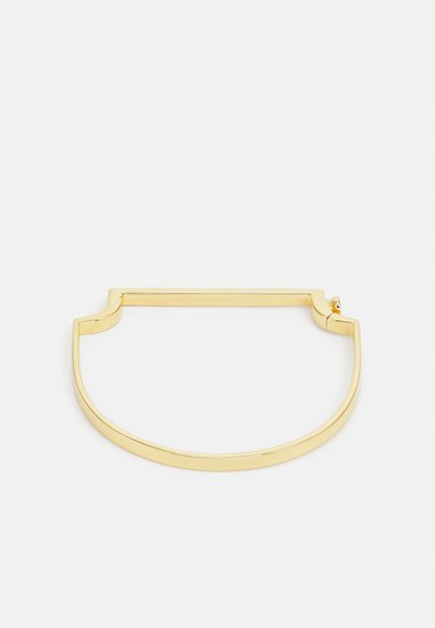 Kuldse tooni metallist käevõru, millel on sile, ümar kuju ja ülal lõikega detail. Minimalistlik disain, millel on poleeritud viimistlus.