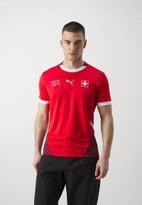Rød kortærmet trøje med hvide accenter, med rund halsudskæring, lodret mønster, Schweiz flag emblem og Puma logo på fronten.