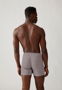 Grijze katoenen boxershorts met een elastische tailleband, van achteren getoond op een mannelijke model. Gladde textuur en aansluitend ontwerp.