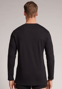Zwarte longsleeve t-shirt van zachte stof, met een ronde halslijn en een ontspannen pasvorm, en stikdetails langs de zoom en manchet.