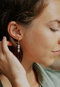 Cercei de tip cerc din aur cu trei perle albe mici, rotunde, atârnând de un lanț delicat, prezentând un finisaj neted și un design elegant.