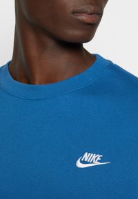 Camiseta de algodón de manga corta azul con escote redondo. Presenta un logotipo de Nike bordado en blanco en la parte delantera. Textura suave.