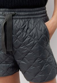 Shorts matelassés de couleur gris foncé avec une taille élastique, un cordon de serrage et des poches latérales. Fabriqués dans un matériau brillant et texturé. Logo de la marque visible.
