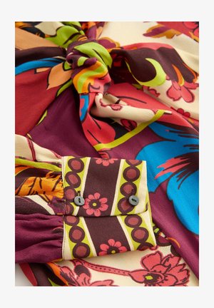 Tkanina sukienki w kwiaty w bogatym burgundzie, kremie i żywych kolorach. Posiada węzeł z guzikiem oraz kieszeń, prezentując wzór w paski.