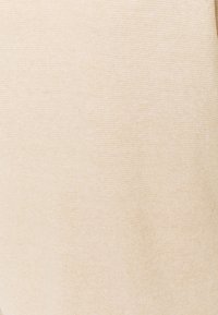 Beige stickad tyg med en mjuk struktur, som har ett subtilt kornmönster. Materialet ser lätt och varmt ut.