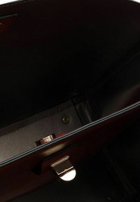 Braune Ledertasche Innenraum mit goldfarbener Hardware und Druckknopfverschluss, ausgestattet mit schwarem Innenfutter und Nähdetails.