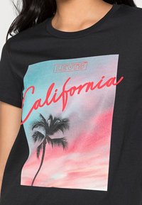 Černé tričko s barevným potiskem palmy a slovem "California" v červené kurzivě, s logem Levi's nahoře.