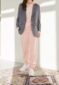 Grå randig blazer över en rosa hoodie, tillsammans med rosa sweatpants och vita sneakers. Outfiten har en avslappnad passform och en avslappnad stil.