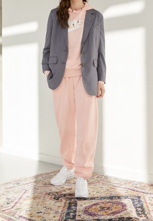 Blazer gris à rayures fines sur un hoodie rose, associé à un jogpant rose et des baskets blanches. La tenue présente une coupe décontractée et un style casual.