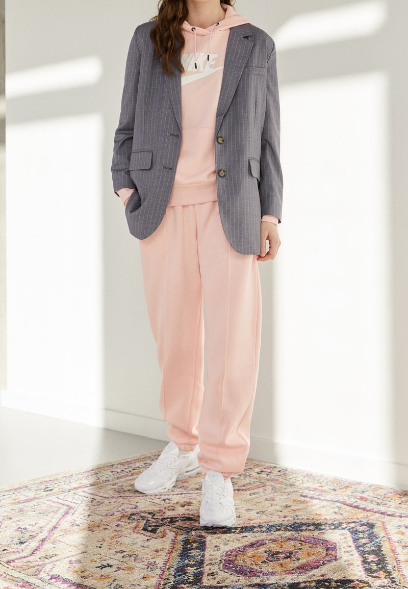 Grå randig blazer över en rosa hoodie, tillsammans med rosa sweatpants och vita sneakers. Outfiten har en avslappnad passform och en avslappnad stil.