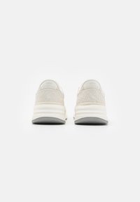 New Balance sneaker világos bézs színben, texturált velúr felsőrésszel, fehér részletekkel, és párnázott középtalppal, szürke talppal.