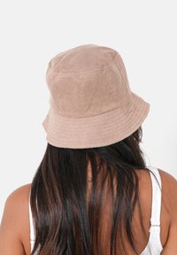 Cappello a secchiello in morbido materiale marrone chiaro con una superficie testurizzata; presenta una visiera ampia e curva e dettagli ricamati sulla corona.