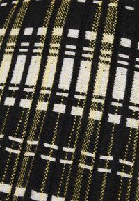 Tessuto nero con un motivo a quadri geometrici in bianco e giallo, con dettagli in maglia testurizzati e larghezze di strisce variegate.