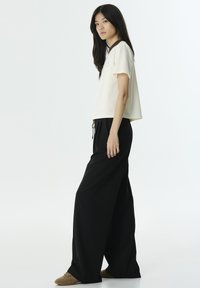 Top a maniche corte color crema con collo rotondo, abbinato a pantaloni neri a gamba larga e scarpe slip-on beige. Design semplice e moderno.