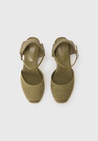 Olivengrønn duk-espadrille-sko med en teksturert vevd ankelrem. Rund tå og flatt hæl med naturlige fiberdetaljer rundt sålen.