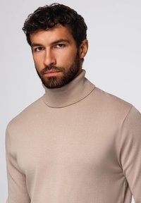 Maglione a collo alto beige realizzato in morbido tessuto a maglia a costine; presenta un collo alto e una silhouette aderente.