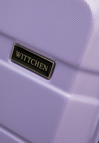 Materiale viola con texture e motivo esagonale. Un'etichetta nera rettangolare con "WITTCHEN" in argento è applicata sulla superficie.