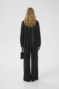 Tuta in satin nero con vestibilità rilassata, dotato di strisce laterali bianche, abbinato a pantaloni larghi e una piccola borsa nera.