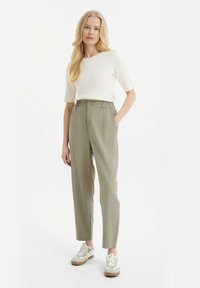Lichtgewicht, geribbelde witte top met korte mouwen, gecombineerd met ontspannen, olijfgroene broek met elastische taille en twee voorzakken.
