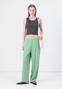 Pilkas trumpas tank top'as, šviesiai žali laisvi kelnių, plokšti juodi batai ir kreminės spalvos petinė maišas. Lygus audinys, kasdieniškas fasonas, atsipalaidavęs dizainas.