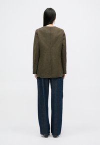 Brązowa marynarka w kratkę houndstooth o dopasowanym kroju, z wyraźnymi ramionami i prostym tyłem. Połączona z ciemnymi spodniami dżinsowymi o szerokich nogawkach.