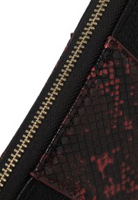 Borsa a mano in pelle nera con un accento testurizzato e decorato in rosso e nero. Chiusura con zip dorata e dettagli di cucitura visibili.