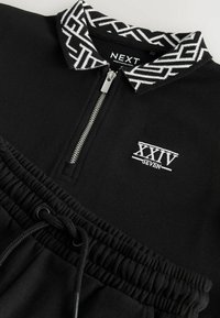 Pullover nero con zip e colletto a fantasia; presenta il logo ricamato "XXIV SEVEN" in bianco e un elastico in vita con cordino.