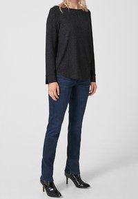 Schwarzes Langarmoberteil mit strukturiertem Finish, kombiniert mit dunkelblauen Jeans. Das Oberteil verfügt über kontrastierende schwarze Manschetten und einen lässigen Schnitt.