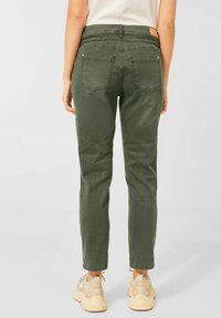 Pantalones verde oliva ajustados con bolsillos traseros, cintura elástica y corte casual. Se combinan con zapatillas beige con detalles en negro.
