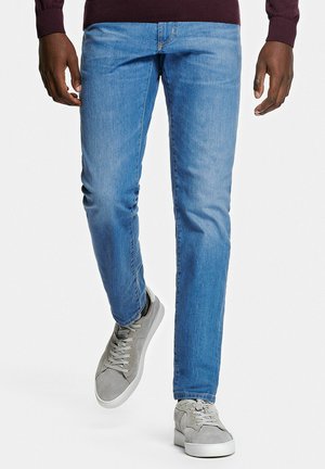 Jean en denim bleu clair à coupe slim, doté d'une texture lisse et d'un léger effet délavé. Associé à des baskets décontractées grises.