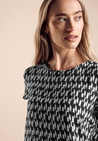 Schwarzes und weißes, gemustertes T-Shirt mit rundem Ausschnitt und kurzen Ärmeln, das aus einem strukturierten Stoff mit abstraktem Design besteht.