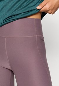 Kõrge vöökohaga legginsid pehmest lilla kangast, millel on tikitud detailid ja mugav elastne vöökoht. Logoga külg.