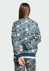 Blommig bomberjacka i mörk marina med vita, blå och gröna mönster, med ribbad mudd och nederkant, lättviktig tyg och avslappnad passform.
