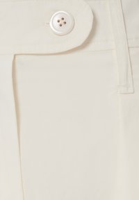 Pantaloni in cotone beige con una superficie liscia, pieghe laterali e un grande bottone bianco in vita.