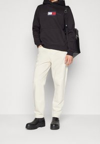 Black hooded sweatshirt with "TOMMY HILFIGER" logo, cream-colored pants, and black ankle boots with a chunky sole.