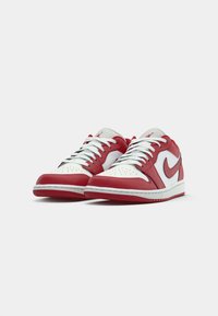 Um par de sapatilhas Nike Air Jordan de cano baixo, vermelhas e brancas, com atacadores brancos e o logo do swoosh da Nike em vermelho, sobre um fundo branco.