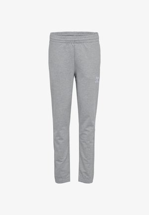 Persona que lleva pantalones deportivos hummel gris claro y zapatillas hummel blancas, caminando con la mano y el torso inferior visibles.